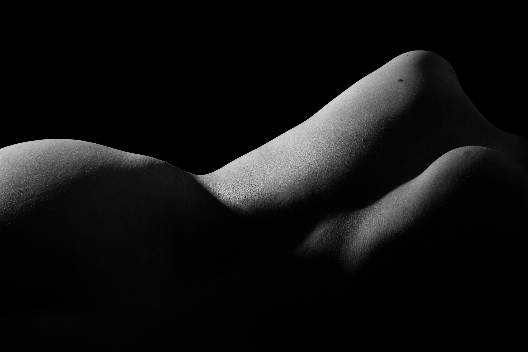 The twins is a black and white abstract view of the human form. Two diagonal shapes that look like mountains rise from the center of the photo and move up and to the right corner. A rounded mountain looking shape covered in shadow can be seen on the left.